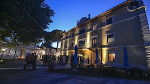 Un'area esterna con tavoli e sedie, un portico coperto e un edificio con numerose finestre e balconi.