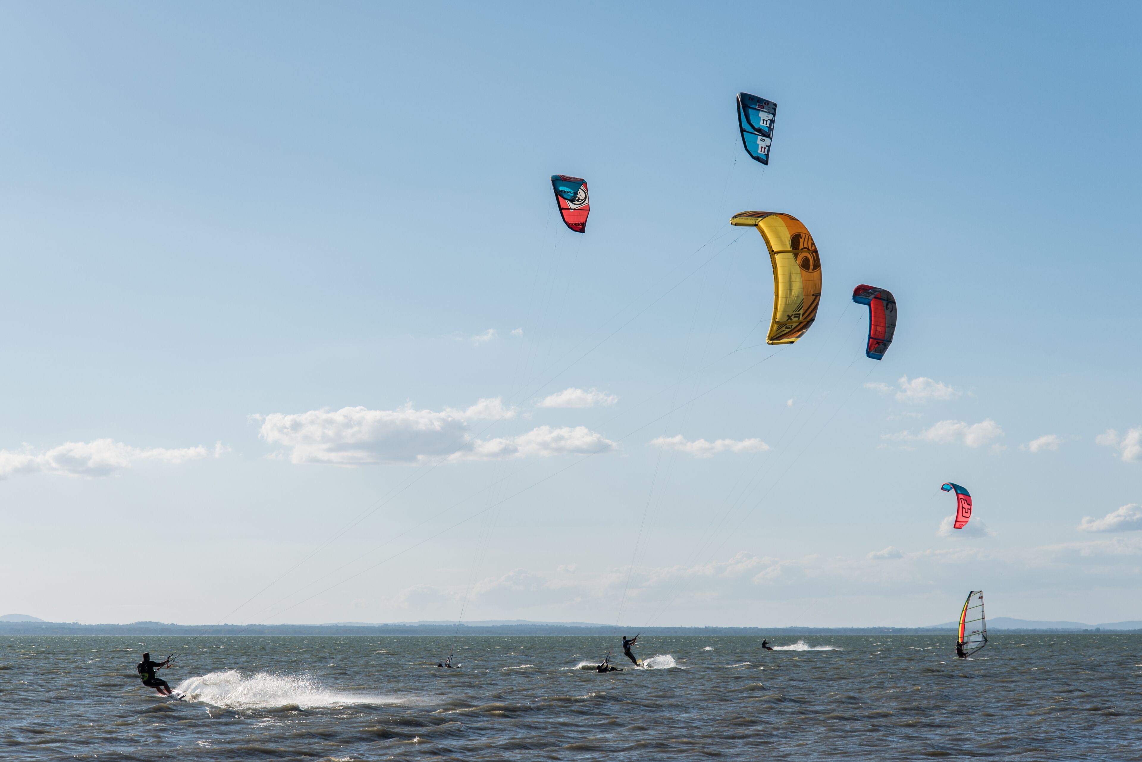 A group of people windsurfing in a body of water with multiple kites in the sky.