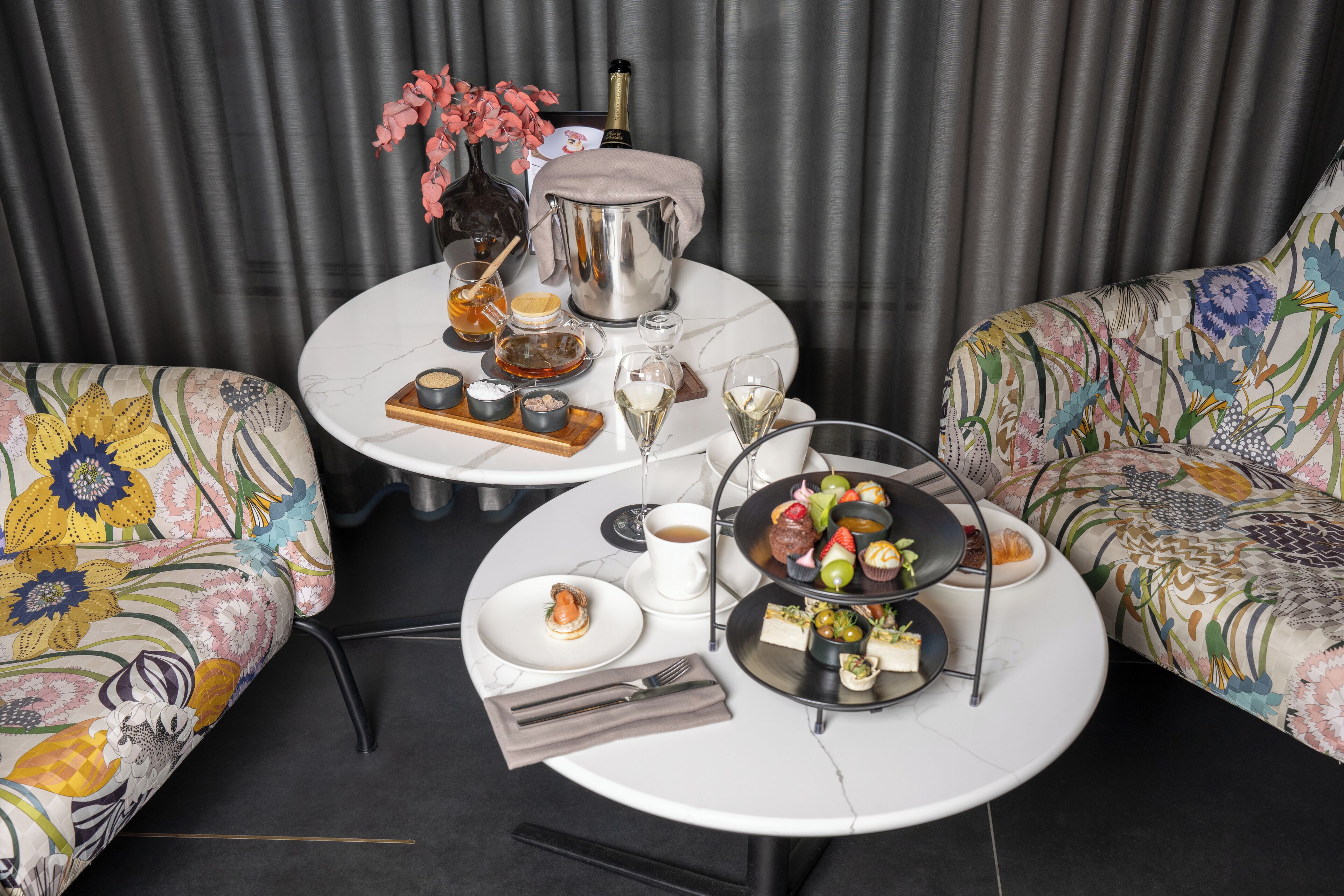 Een eettafel gedekt met een taartstandaard met drie verdiepingen, een champagnefles en een vaas met bloemen.