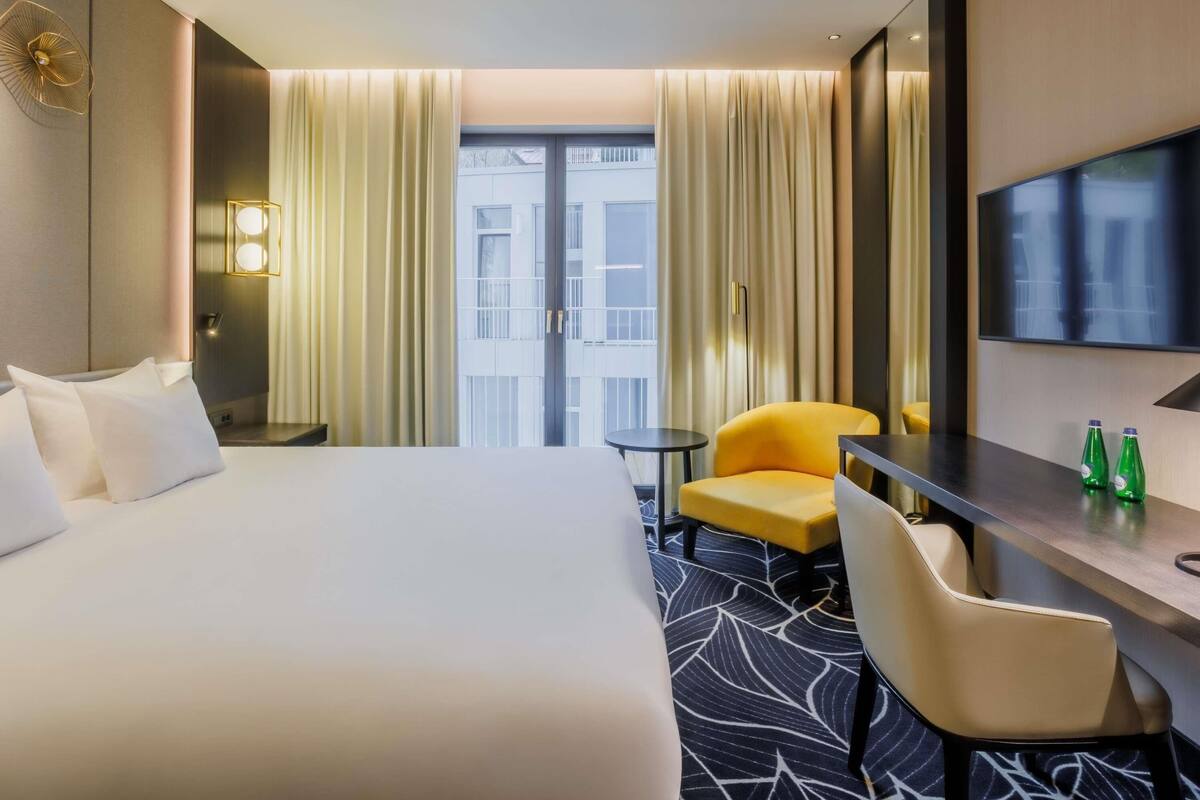Ein Hotelzimmer mit Bett, Schreibtisch, Stuhl, Fernseher und Blick ins Freie.