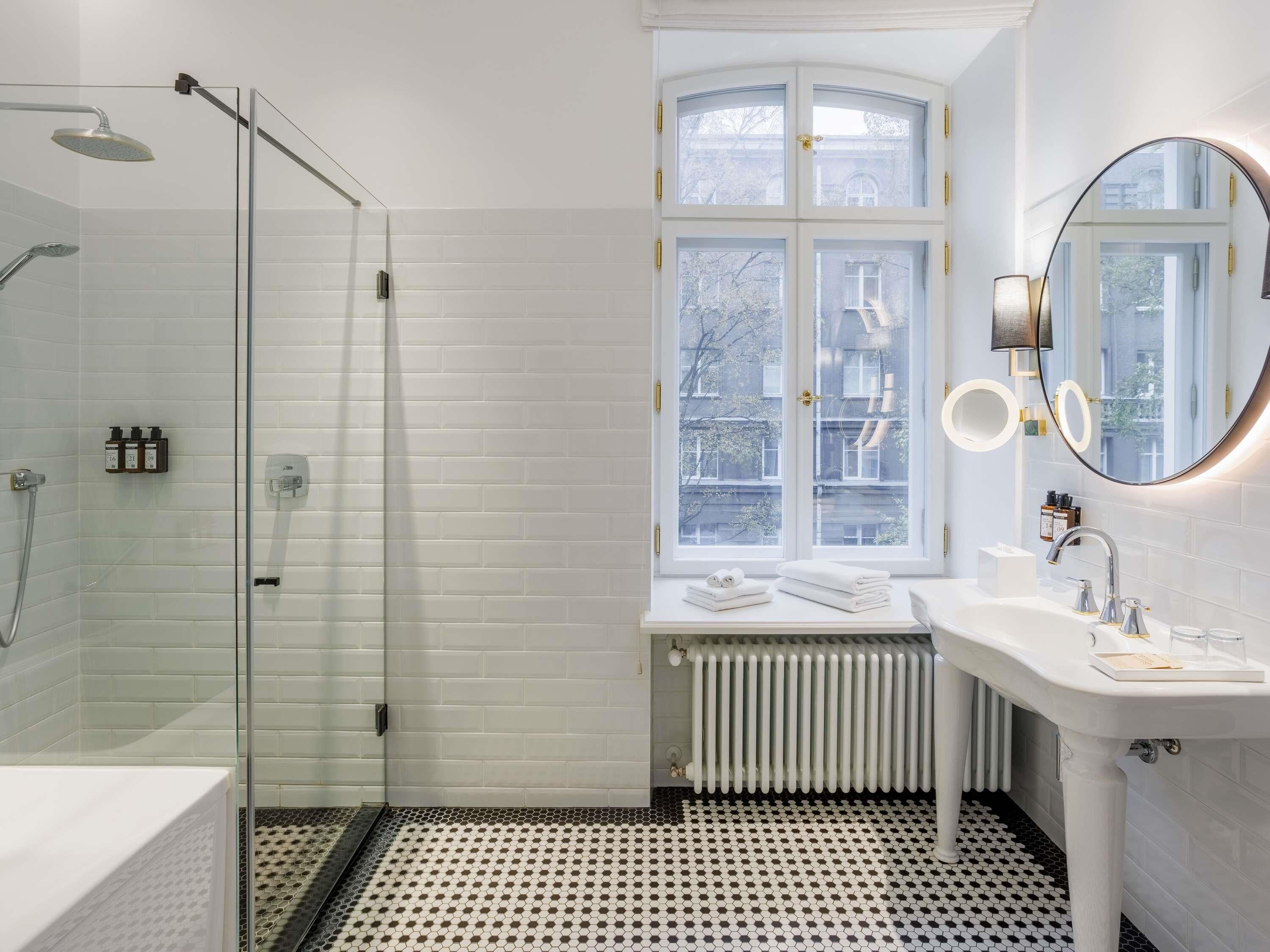 A modern bathroom with a glass shower enclosure, a white sink with a mirror, and a window with a view of the outside.