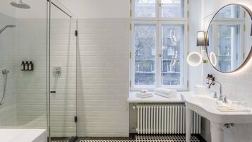 A modern bathroom with a glass shower enclosure, a white sink with a mirror, and a window with a view of the outside.