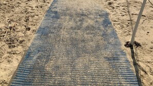 A beach with a blue patterned mat, a wooden structure, and a utility box.