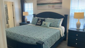 A bedroom with a bed, two bedside tables, a nightstand, a door, and a window with blinds.
