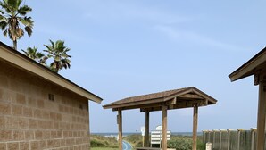 A patio area with a gravel path leading to a wooden pergola, a brick wall, and a view of the ocean.