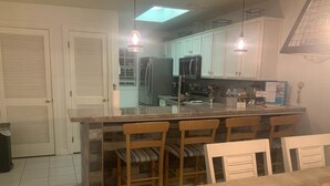 A kitchen with a central island, wooden chairs, a dining table, and white cabinets.