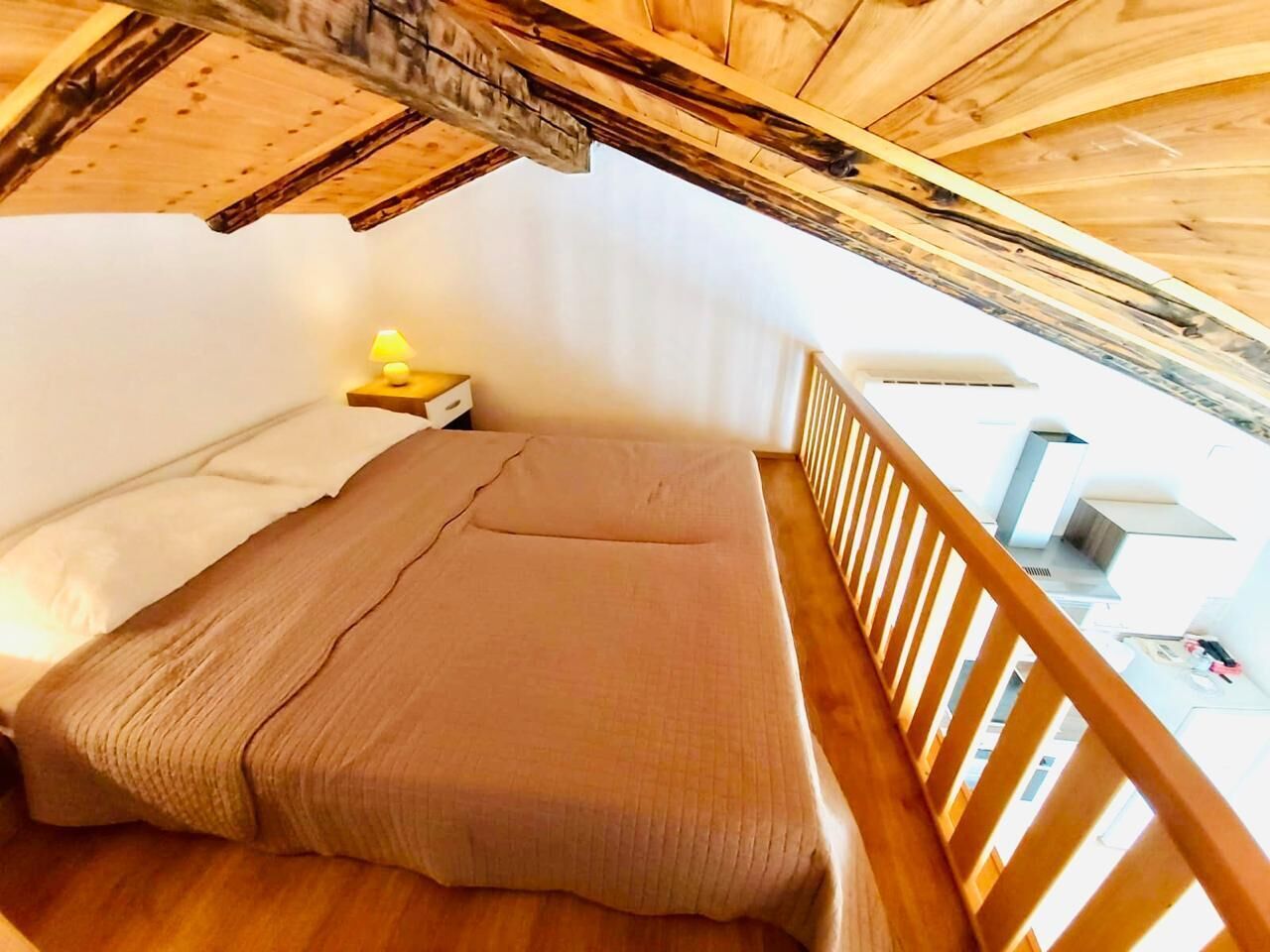 Una cama individual con cabecera de madera en una habitación con paredes blancas y techo inclinado.