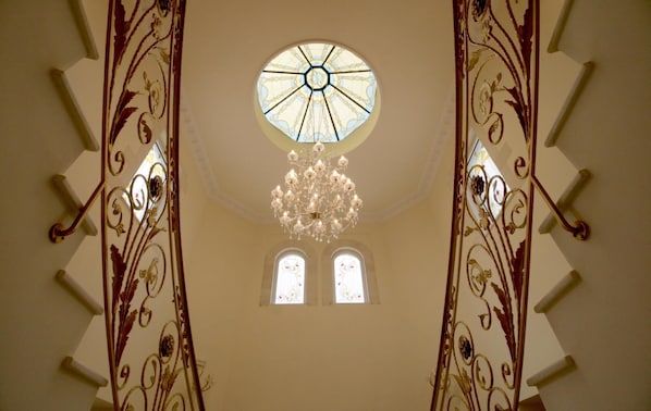 Eine prächtige Treppe mit aufwendiger Metallreling, ein großes rundes Buntglasfenster und eine Chandelüstere.