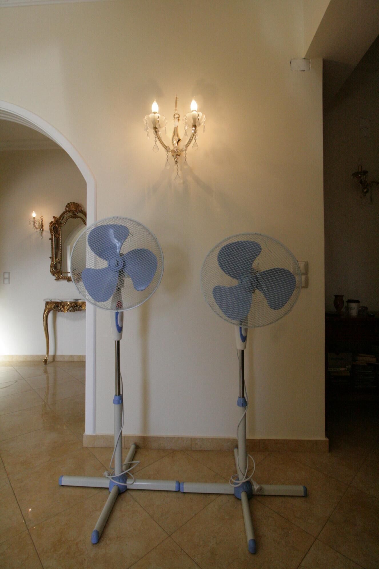 Zwei Standventilatoren in einem Raum mit einer Kandelaber und einem Spiegel.