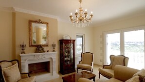 A living room with a fireplace, a chandelier, and two armchairs. - Luxurious Villa Anthi (Chania)