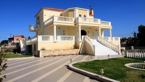 A multi-story building with a central staircase, balconies, and a stone base. - Luxurious Villa Anthi (Chania)