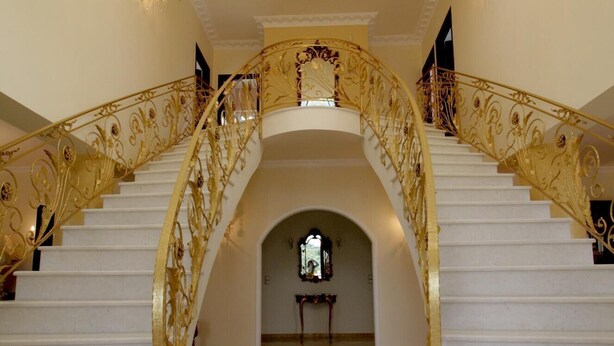 A grand staircase with ornate golden railings and a chandelier. - Luxurious Villa Anthi (Chania)