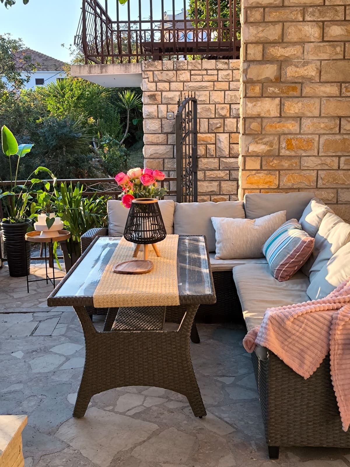 An outdoor patio with a wicker table, a cushioned sofa, and a stone wall.