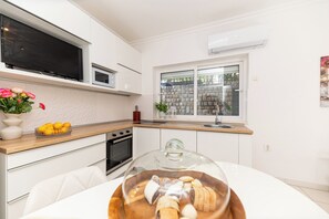 Una cocina moderna con armarios blancos, horno integrado, microondas y un amplio ventanal con vistas a un muro de piedra.