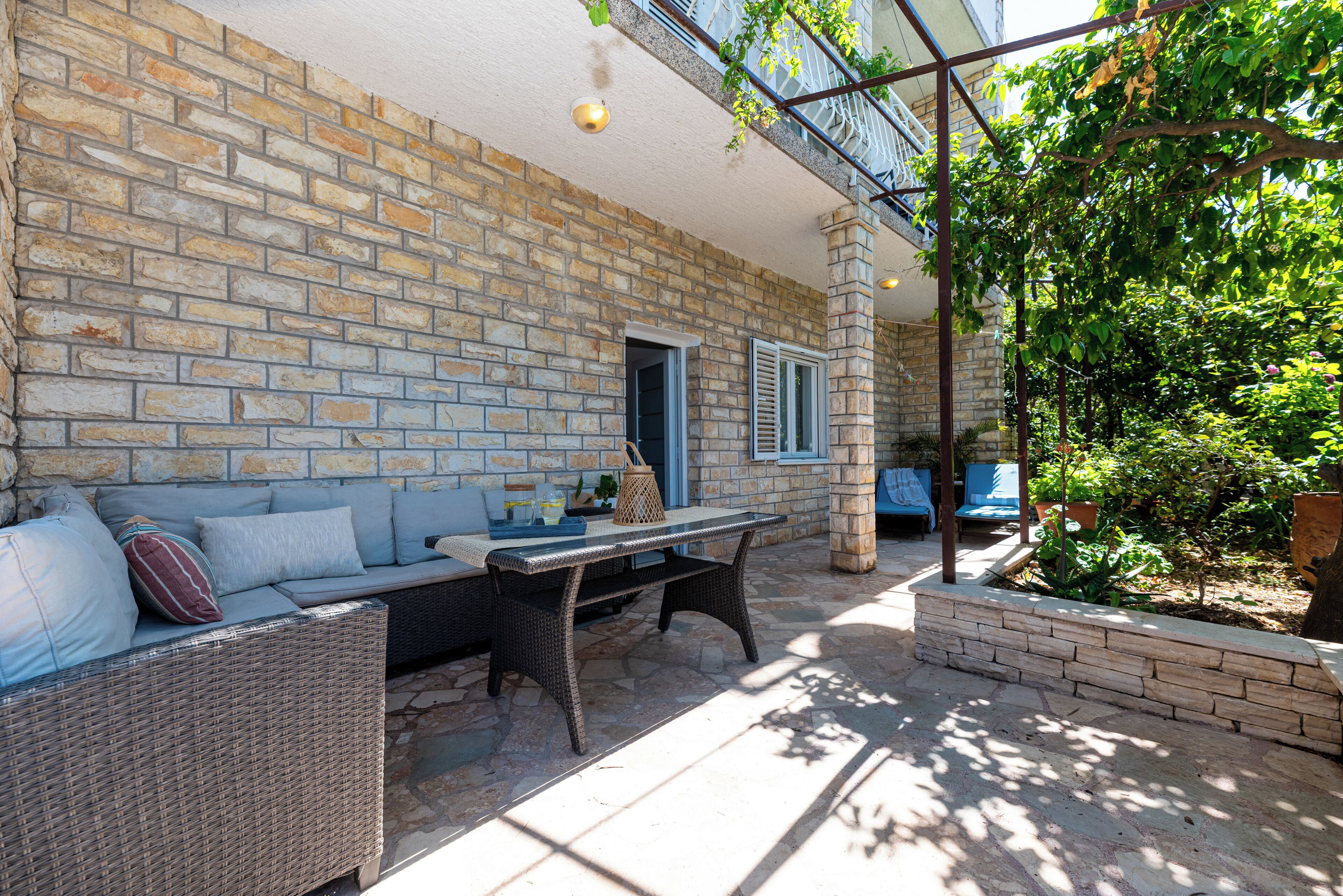 A stone wall, a wicker sofa, a table, and a small garden area.