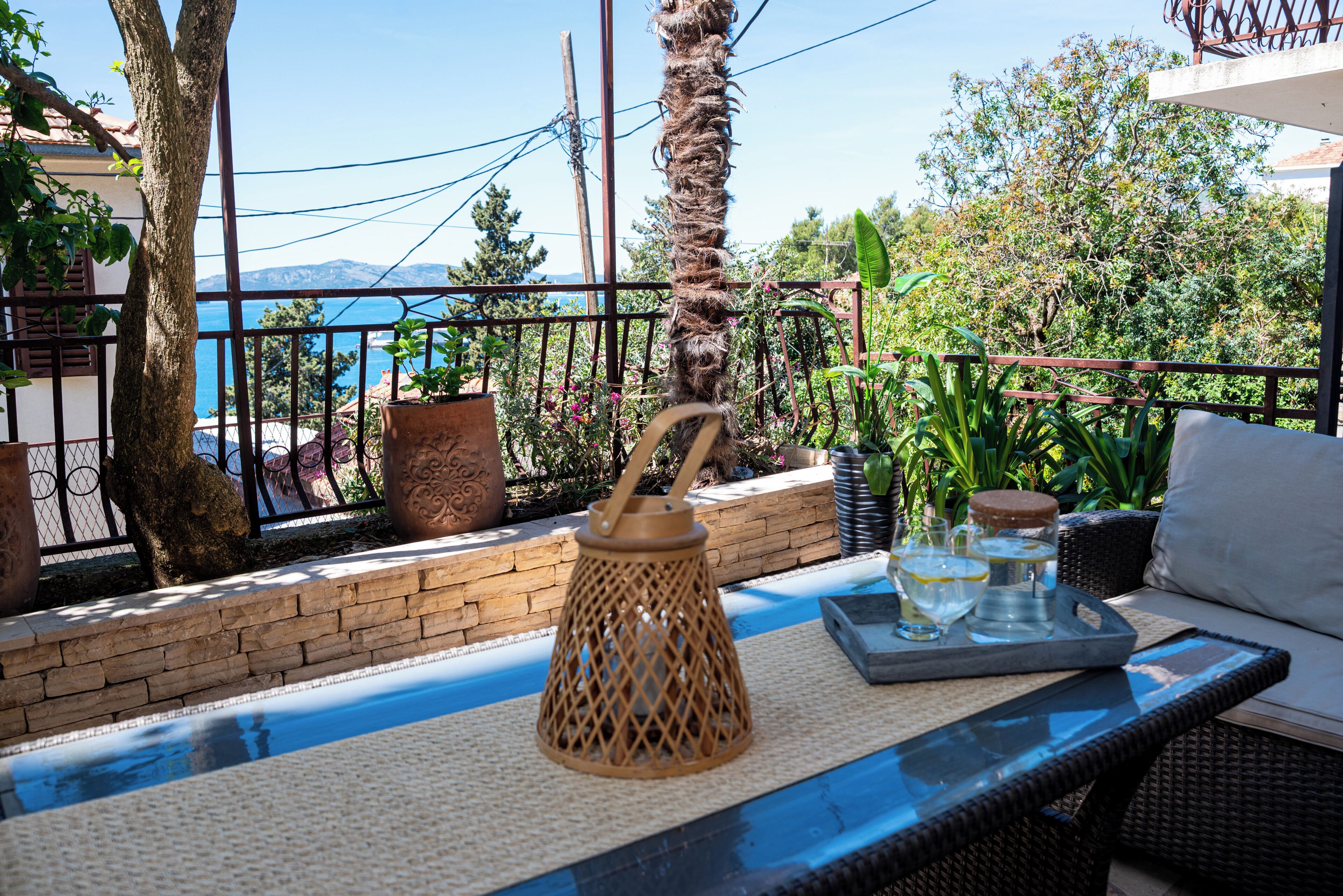 A balcony with a wicker chair, a table with a tray, and a view of the sea.