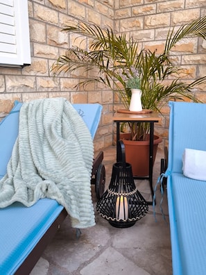 A small patio area with two blue lounge chairs, a white knitted blanket, a potted plant, and a black lantern.