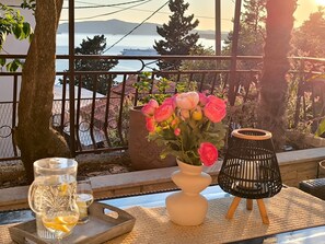 Un balcon avec vue sur la mer, un vase de fleurs, un verre et une lampe noire.
