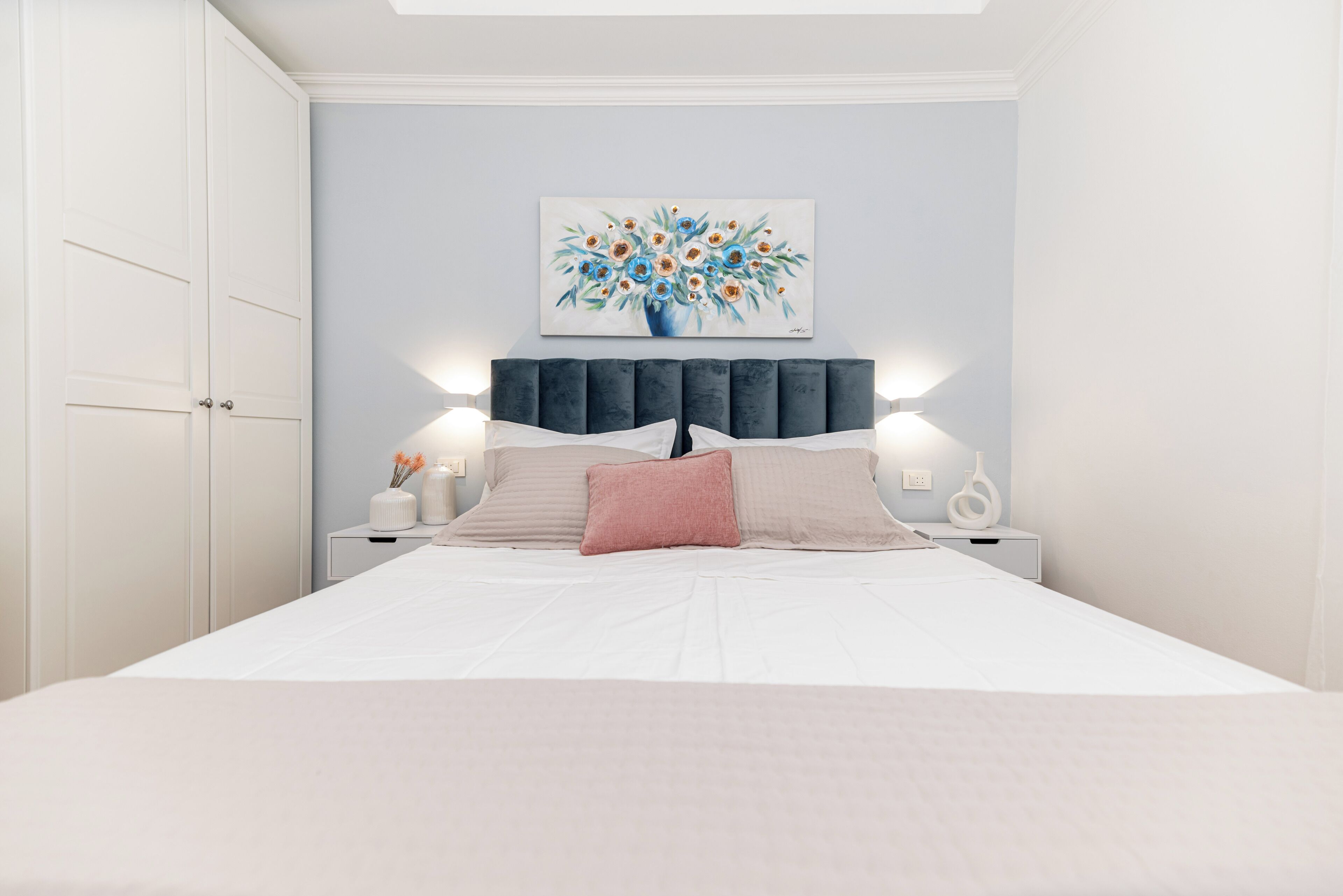 Cama bem arrumada com cabeceira, mesas de cabeceira e uma obra de arte na parede.
