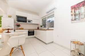 Una cocina moderna con armarios blancos, horno empotrado, microondas y ventana con vista a una pared de piedra.