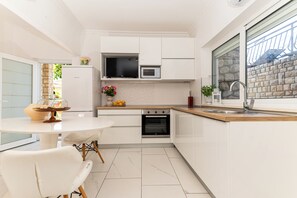 A modern kitchen with white cabinetry, a built-in oven, a microwave, and a window with a view of a brick wall. - Apartment With Amazing sea View (Trogir)