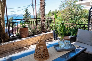 A balcony with a view of the sea, a wicker sofa, a tray with glasses, and potted plants. - Apartment With Amazing sea View (Trogir)