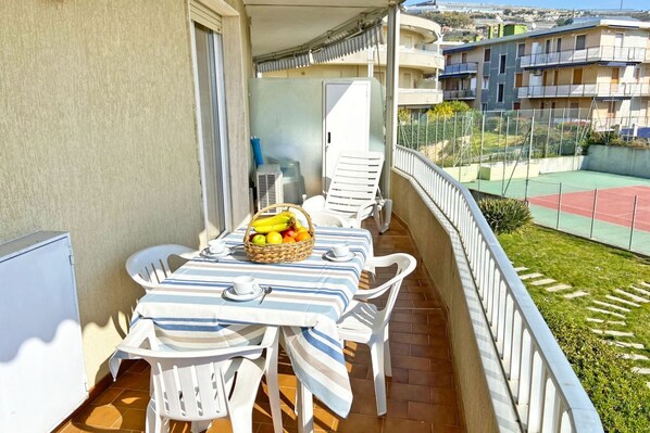 Enjoy a meal on the balcony with a view of the tennis court and surrounding buildings.