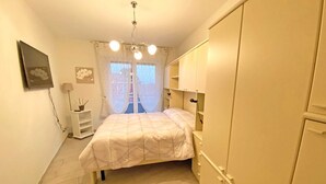 A bedroom with a bed, a wardrobe, a bedside table, and a window with curtains. - TWO-ROOM APARTMENT with balcony 50 meters from the SEA and 7 KM from SANREMO (Santo Stefano al mare)