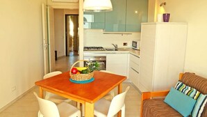 A compact kitchen with a dining table and chairs, a basket of fruit, and a sofa with cushions. - TWO-ROOM APARTMENT with balcony 50 meters from the SEA and 7 KM from SANREMO (Santo Stefano al mare)