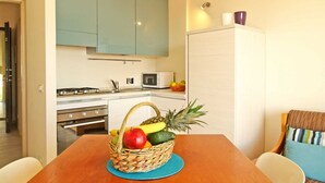 A kitchen with teal cabinets, a microwave, and a fruit basket on the table. - TWO-ROOM APARTMENT with balcony 50 meters from the SEA and 7 KM from SANREMO (Santo Stefano al mare)