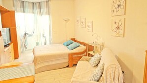 A bedroom with two single beds, a wooden wardrobe, a desk, a chair, and a sofa. - STUDIO APARTMENT with balcony 50 meters from the SEA and 7 KM from SANREMO (Santo Stefano al Mare)