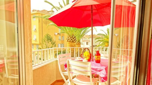 A balcony with a red umbrella, white chairs, and a table with a pink tablecloth. - STUDIO APARTMENT with balcony 50 meters from the SEA and 7 KM from SANREMO (Santo Stefano al Mare)