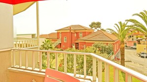 A balcony with a red umbrella, a white railing, and a view of red buildings and palm trees. - STUDIO APARTMENT with balcony 50 meters from the SEA and 7 KM from SANREMO (Santo Stefano al Mare)