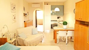A compact living space with a kitchenette, a dining area, and a sofa with pillows. - STUDIO APARTMENT with balcony 50 meters from the SEA and 7 KM from SANREMO (Santo Stefano al Mare)