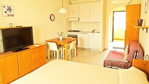 Ein kleines Hotelzimmer mit Bett, Fernseher, Esstisch mit Stühlen, einer Küchenzeile und einem Badezimmer mit Dusche.