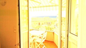 Ein offener Balkon mit Tisch und Stühlen, der auf einen Wohnbereich und ein Gewässer blickt.