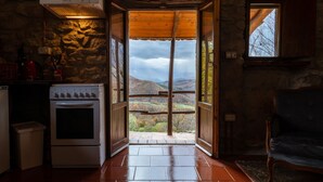 A rustic kitchen with a stone wall, a stove, and a view of a mountainous landscape through an open door. - Novanta (Bibbiena)