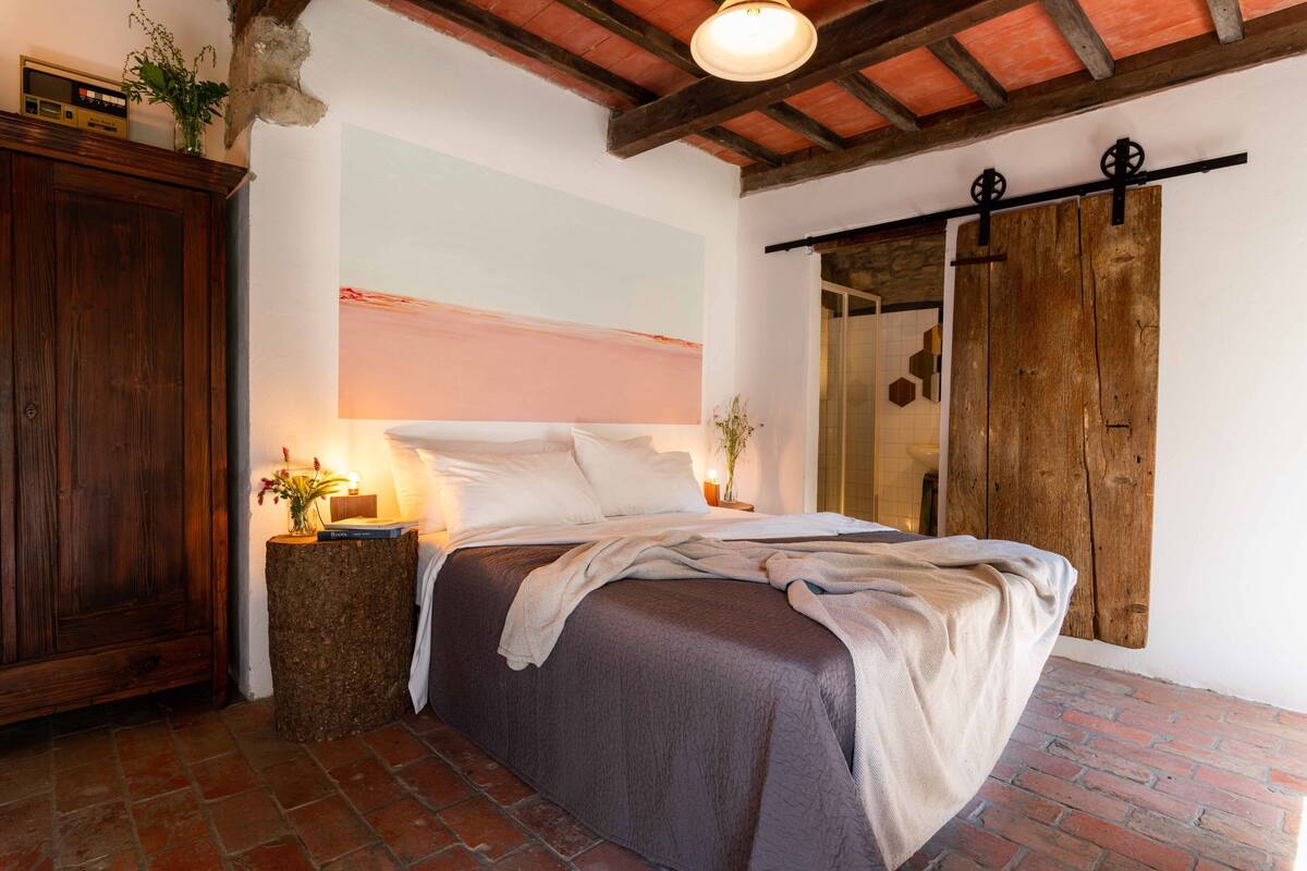 Un dormitorio con una cama grande, un armario de madera, suelo de ladrillo rústico y techo con vigas a la vista.