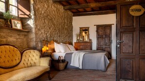 A rustic room with a stone wall, a bed with a grey bedspread, a wooden bench, and a wooden door labeled "CALAVANDA". - Novanta (Bibbiena)