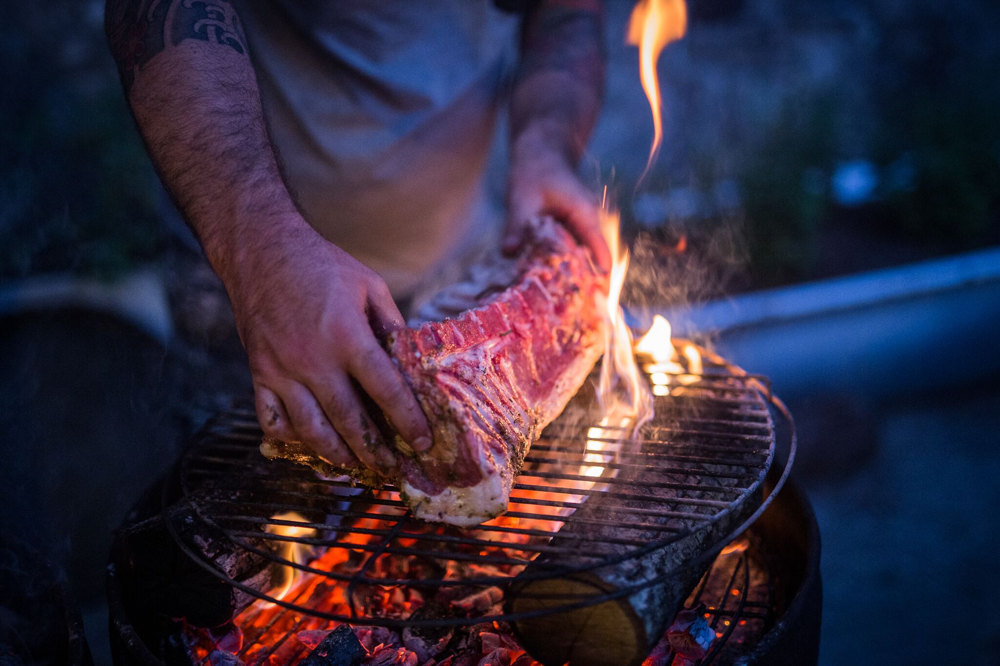Una persona asando un trozo grande de carne en una parrilla al aire libre.