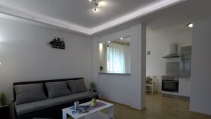 A modern living room with a grey sofa, a white coffee table, and a small ottoman. There is a kitchen area with a stove and cabinets visible. - Comfortable Apartment in Stari Grad (Stari Grad)