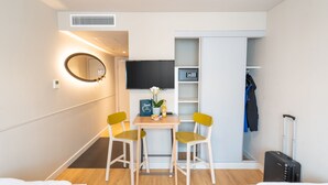 A hotel room with a bed, a desk with two chairs, a television, a mirror, a wardrobe, and a suitcase.