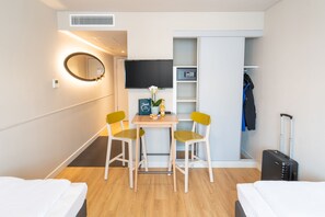 Habitación de hotel con cama, escritorio con dos sillas, televisor, espejo, armario y maleta.