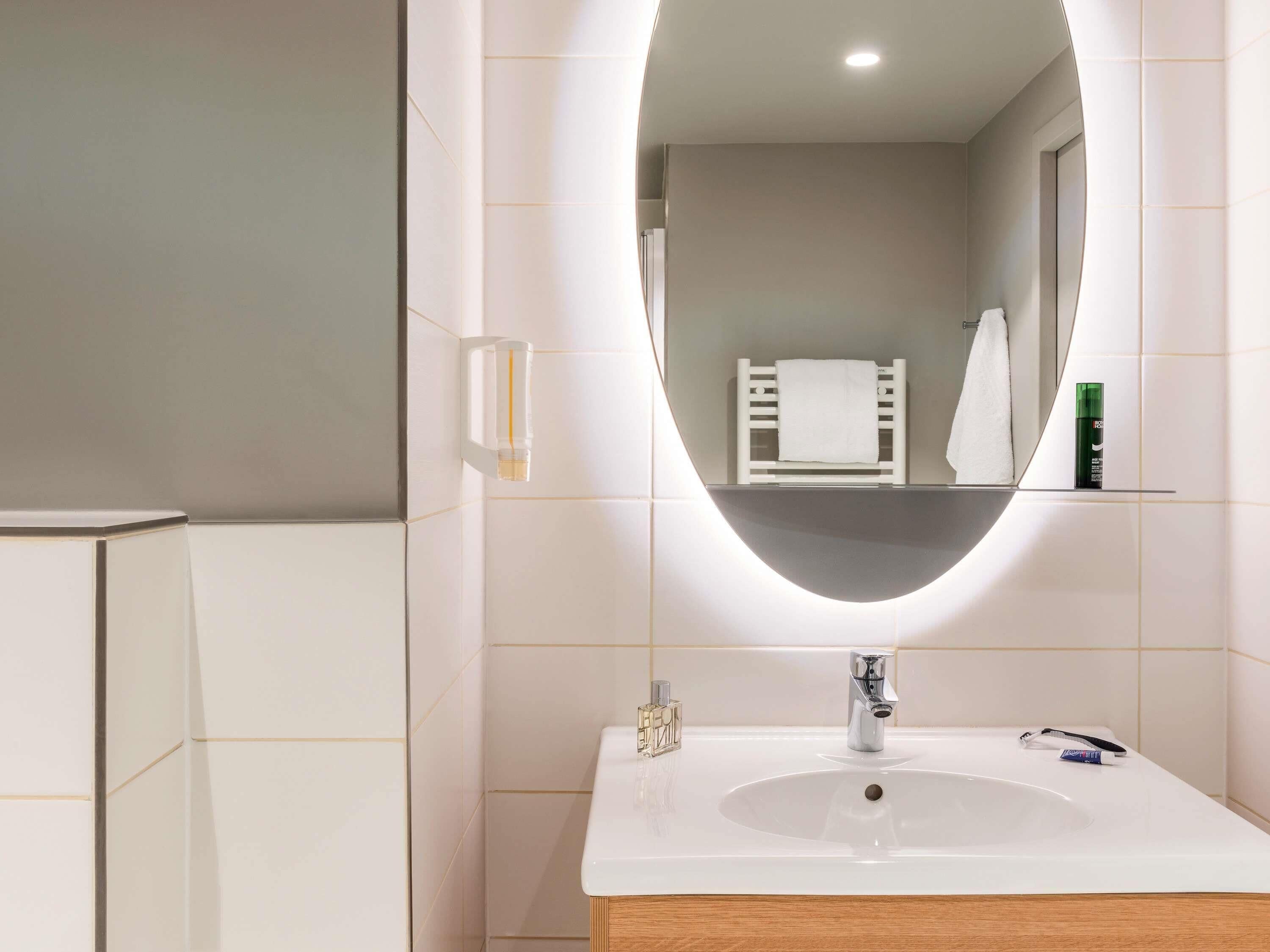 Un baño con un lavamanos blanco, un espejo y un perchero para toallas.