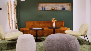 A modern interior with a green wall, a wooden shelf with decorative items, a sofa, and two round tables with chairs.