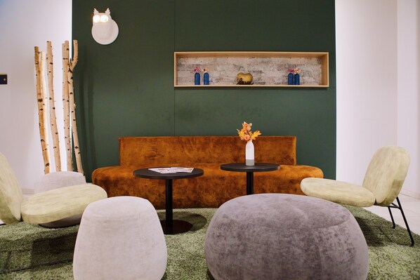 Un interior moderno con una pared verde, un estante de madera con objetos decorativos, un sofá y dos mesas redondas con sillas.