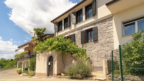 A two-story house with a stone facade, multiple windows with shutters, and a small balcony with plants. - Luxurious Villa in Ružići Croatia With Private Pool and Garden (Matulji)