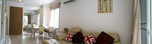 A living room with a sofa, a dining area with chairs and a table, and a kitchen in the background.