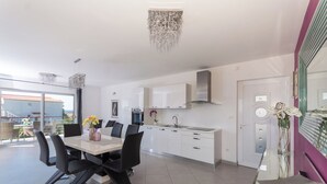A modern kitchen with white cabinets, a stainless steel range hood, and a dining area with a white table and black chairs. - In Center Near the Marina and Beach With Amazing View (Tribunj)