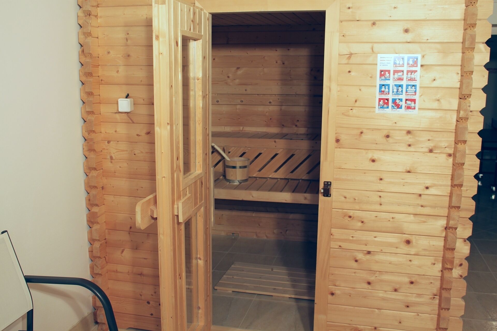 Een houten sauna met een open deur, een houten bank en een poster aan de wand.